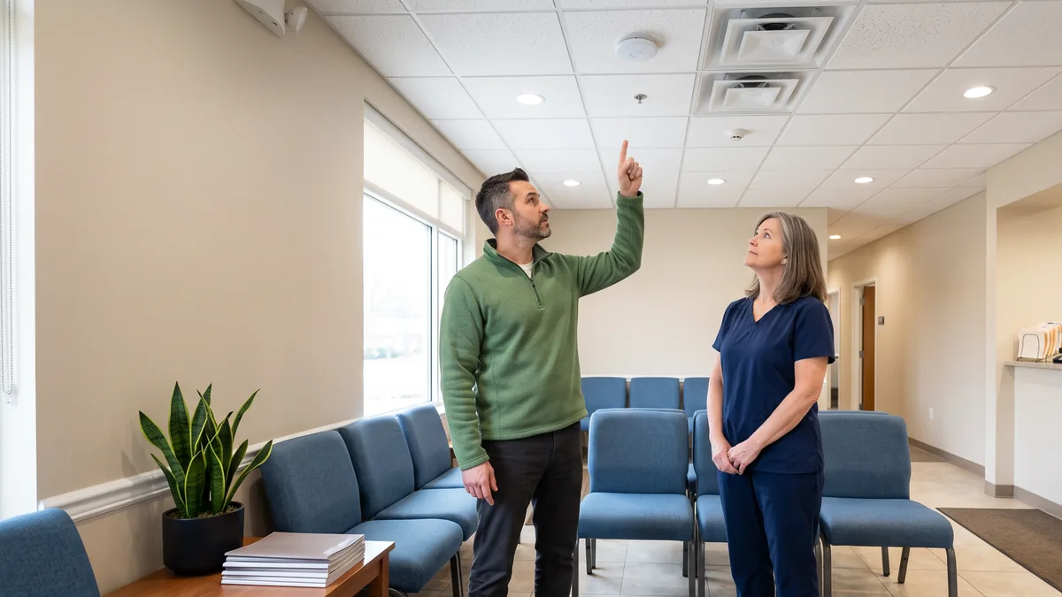 IT consultant pointing to a ceiling wireless access point in a dental office waiting room with the office manager