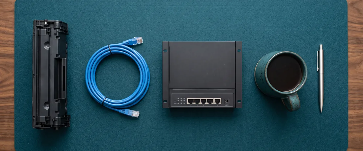 Toner cartridge, ethernet cable, network switch and coffee mug laid out to show what an IT support contract in Rockland County covers